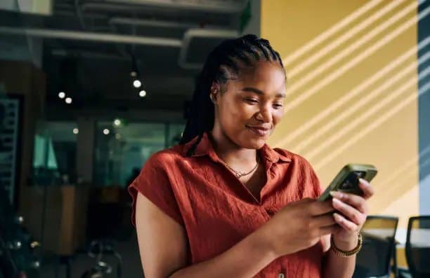 Une femme sourit en lisant un SMS sur son téléphone